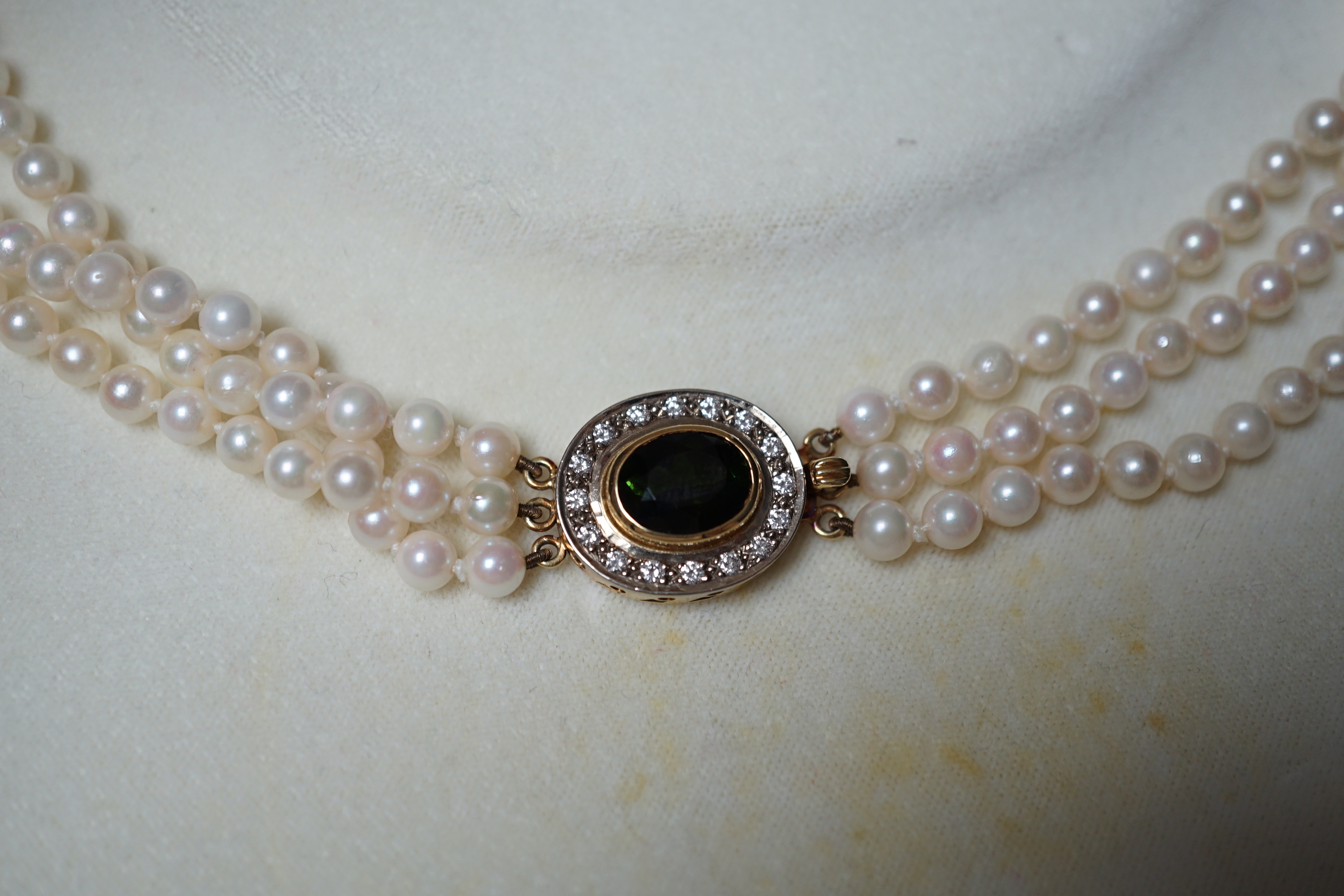 A modern triple strand cultured pearl necklace, with green tourmaline and diamond cluster set oval yellow metal clasp, 48cm.